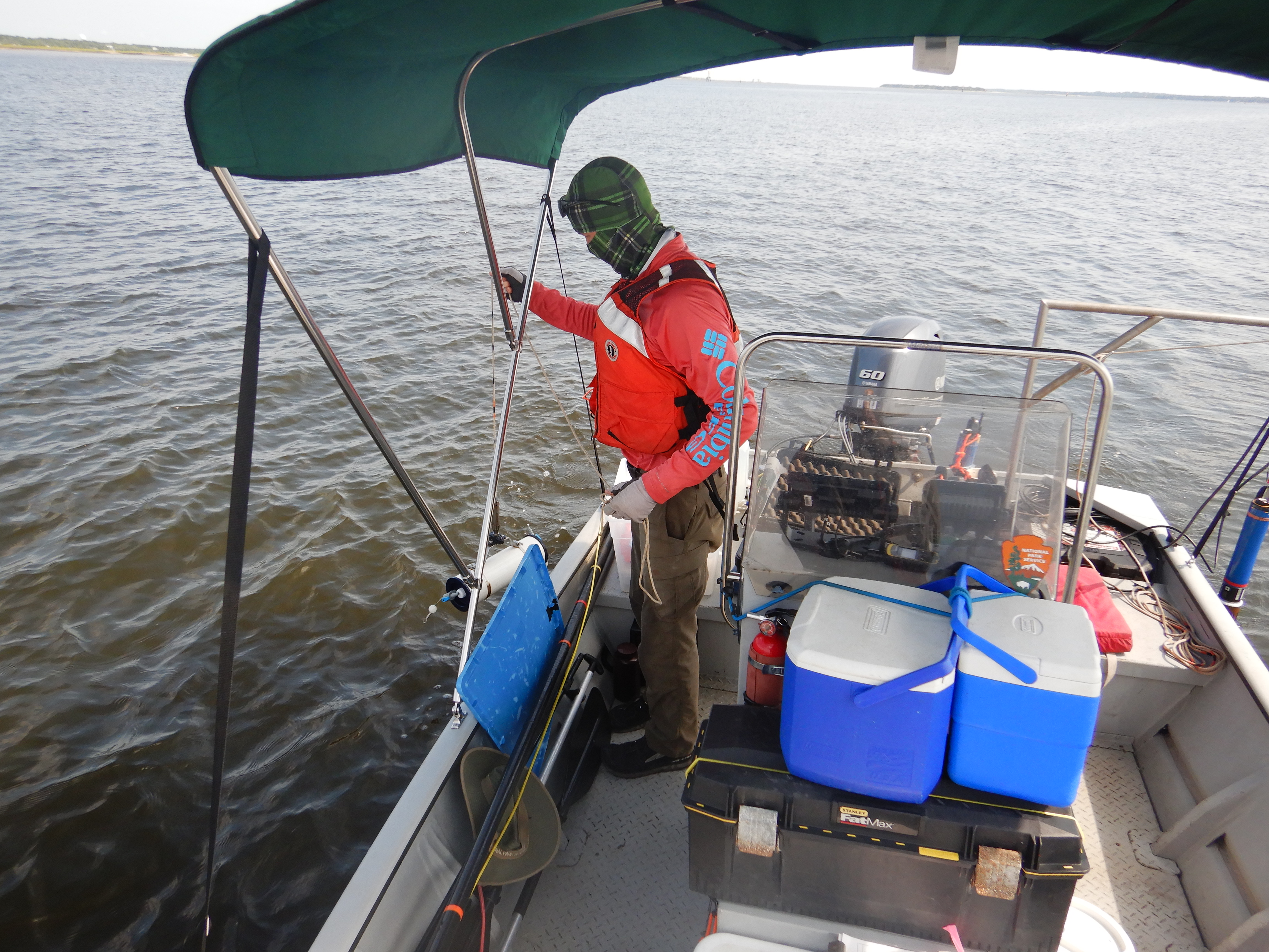 Man in life vest holding a sampler over the side of the boat