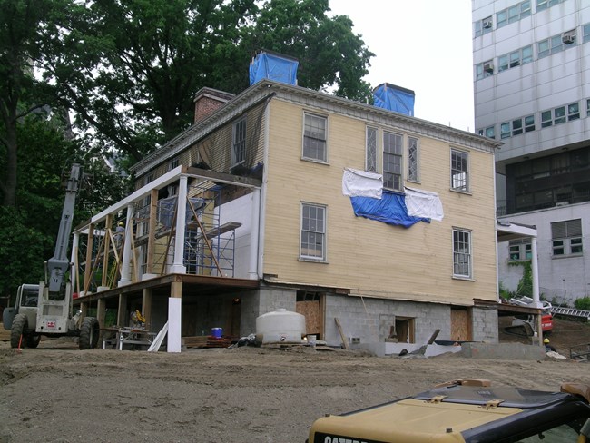 The Grange sits at its new location in 2008, recently moved. Its paint is dull, and it is wrapped in tarp in some locations. The porches are halfway constructed.