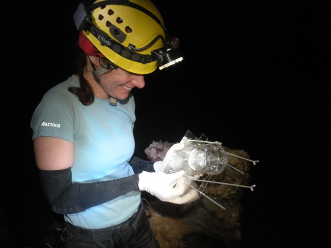 a scientist in caving clothes holds a water filter in a dark cave room