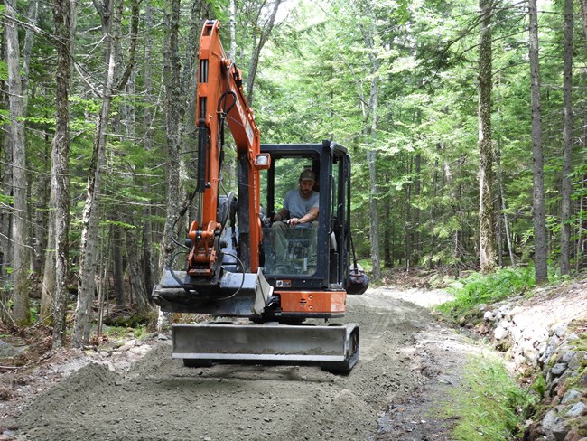 In a large piece of machinery, a park staff member smooths the gravel road surface