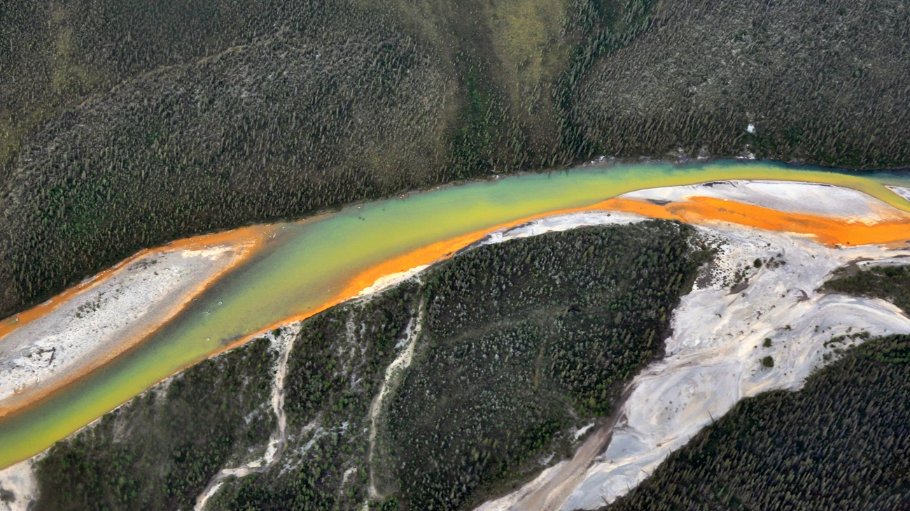 Partially orange river Aerial view of a braided river flowing from right to left. One braid entering the main channel is a bright, solid orange. Another is a yellow hue, where the orange has been diluted. A third is half yellow and half clear, dark water.