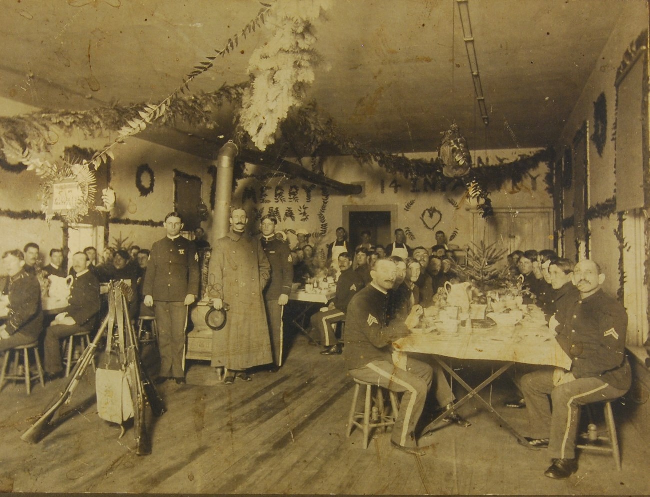 A black and white photo of soldiers sitting inside a room decorated for Christmas.