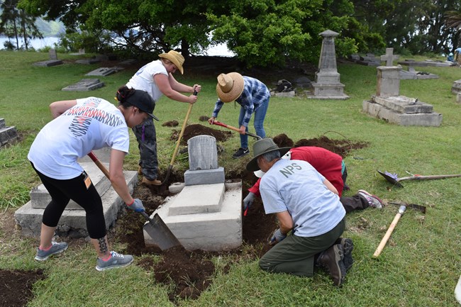 Workshop participants begin the process of leveling a concrete grave marker. Workshop participants begin the process of leveling a concrete grave marker.