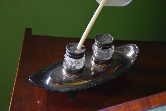 A silver inkstand with a feather pen in it.