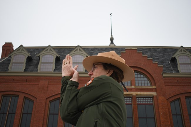 A Ranger twists her arms for a eagle pose. A eagle weather vane sits in the background atop a clock tower.