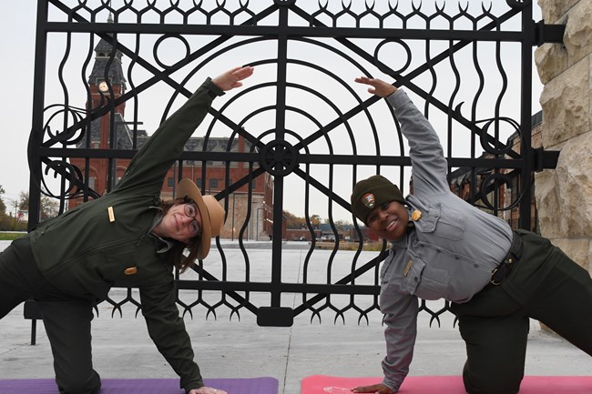 Two rangers practice gate pose in front of a decorative iron gate.