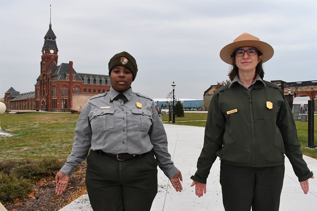 Two Rangers stand in mountain pose in front of the red brick Administration Clock Tower Building.