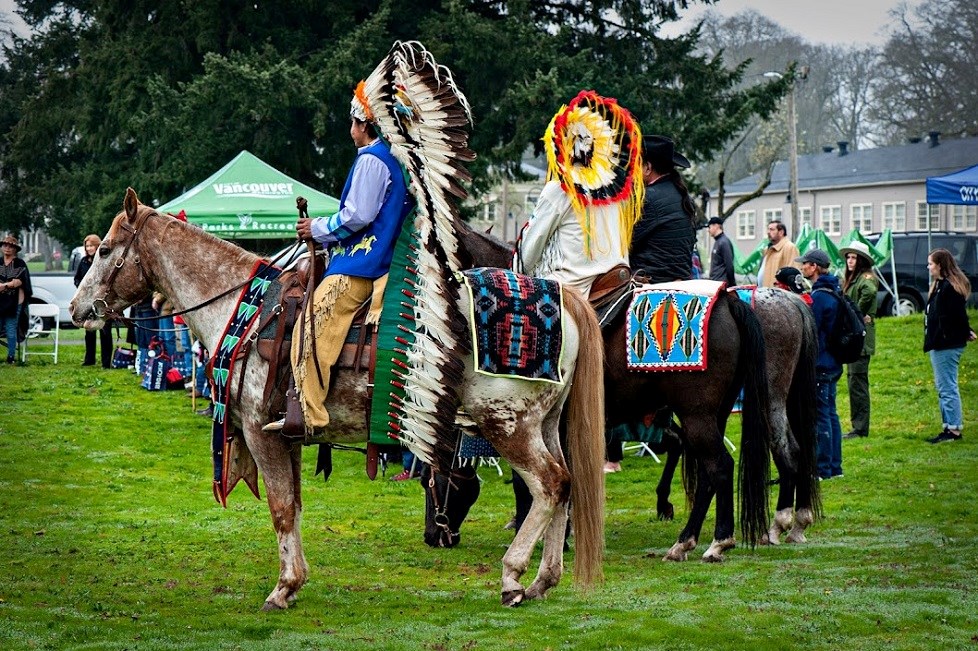 Riders at Chief Redheart Ceremony Two men sit atop horses. The men wear full headresses and regalia.