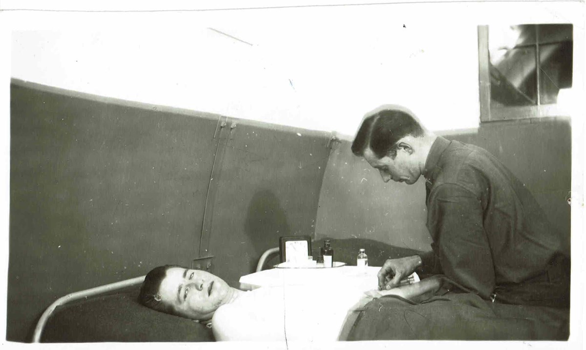black and white photo of a man bending over another man in hospital bed.