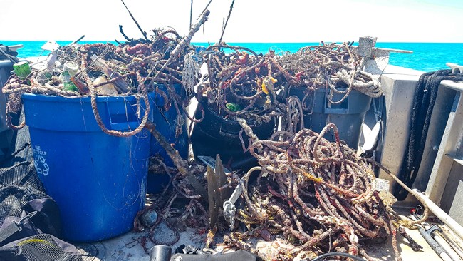 Large trash bins full of various types of marine debris such as fishing line, bottles, and anchors.