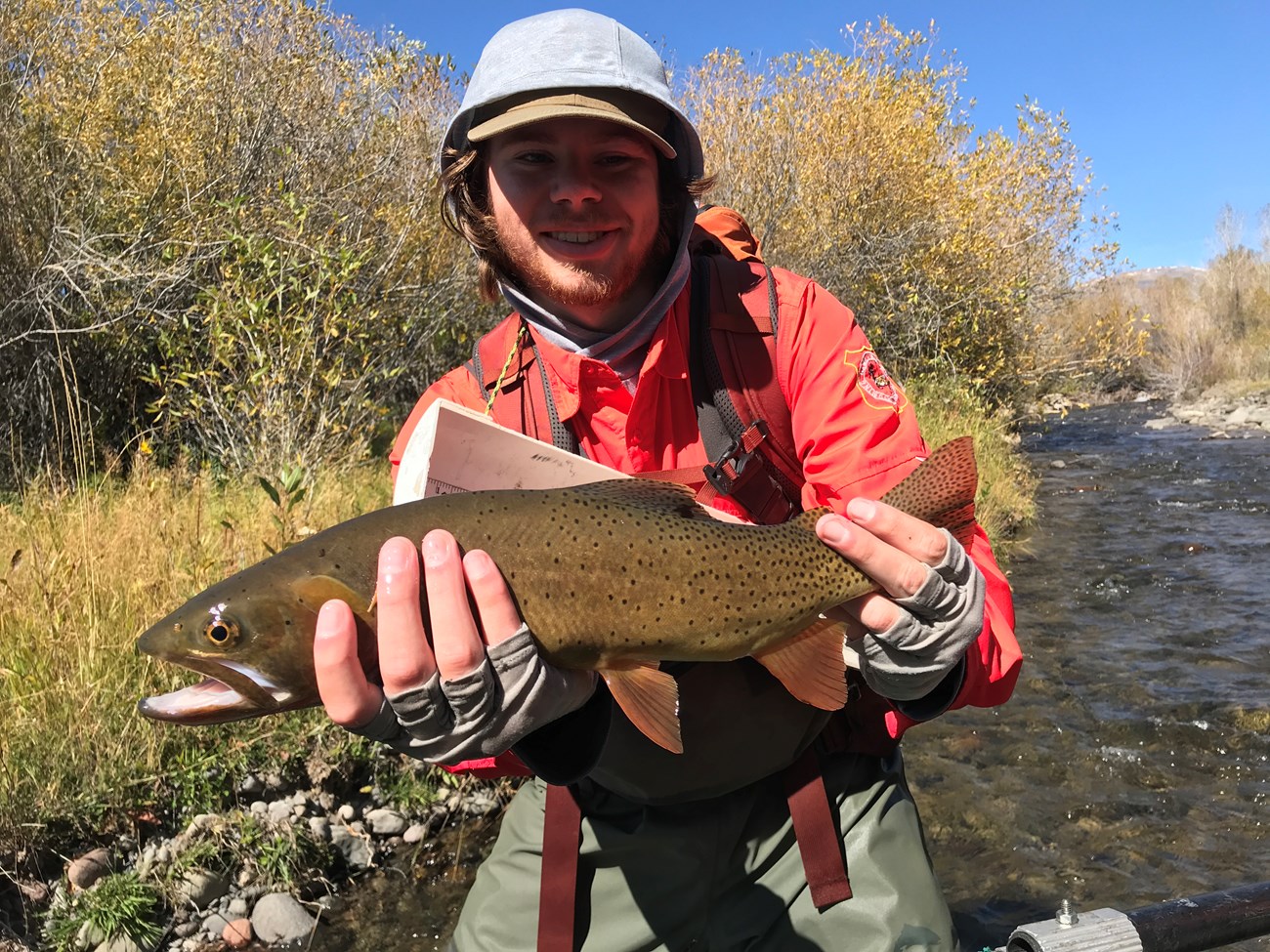 Young man smiling and holding a large, live spotted trout.