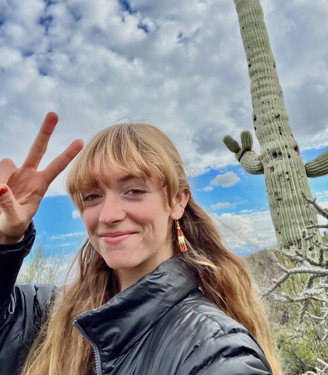 Saguaro National Park Community Volunteer Ambassador Darien Parris-Austin A young woman standing in front of a cactus holding two fingers up in a peace sign