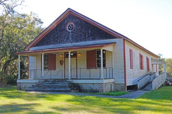 Large one story white wooden building with a red roof and open front porch