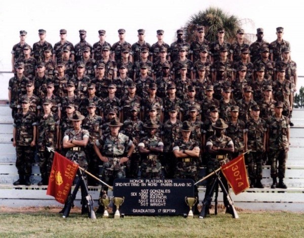 People in uniform standing on riser. Two Marine Corps flags flank the group