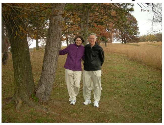 Two people pose arm and arm near a tree.