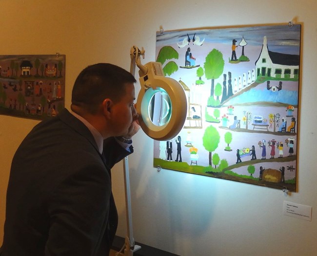 FBI Special Agent Randy Deaton examines a Toye forgery of a Clementine Hunter painting. FBI Special Agent Randy Deaton examines a Toye forgery of a Clementine Hunter painting.