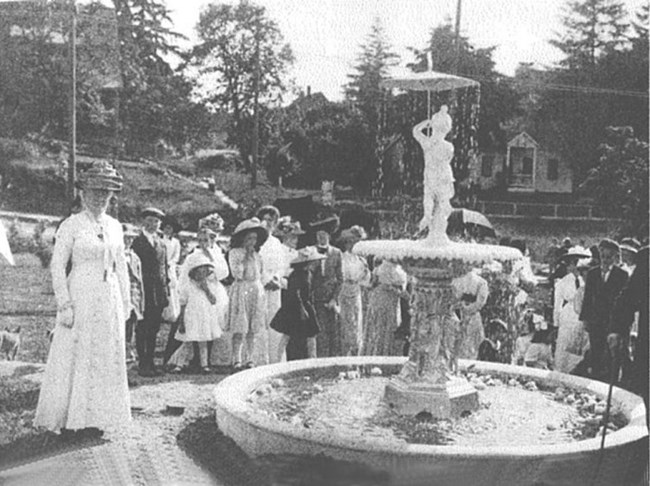 A black and white photo of a group of women and some girls standing around a fountain.