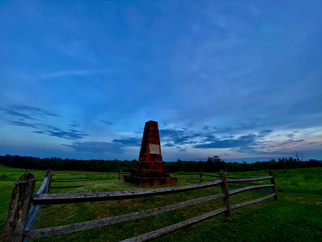 Deep Cut Monument stands in foreground, sunsetting in the distance behind treeline