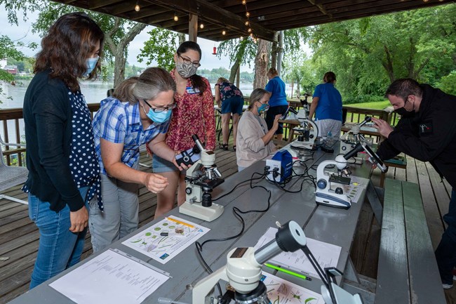 Students wearing masks use microscopes in a covered outdoor floating classroom