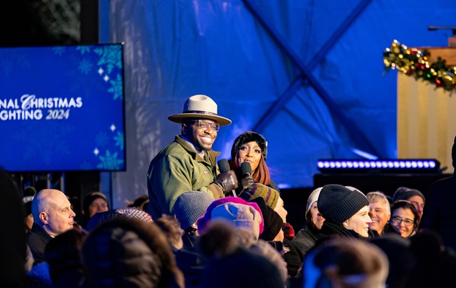 Dexter Armstrong at 2024 National Christmas Tree Lighting A smiling park ranger speaks with the event host in front of a large audience.
