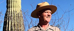 Man in NPS uniform standing next to saguaro cactus