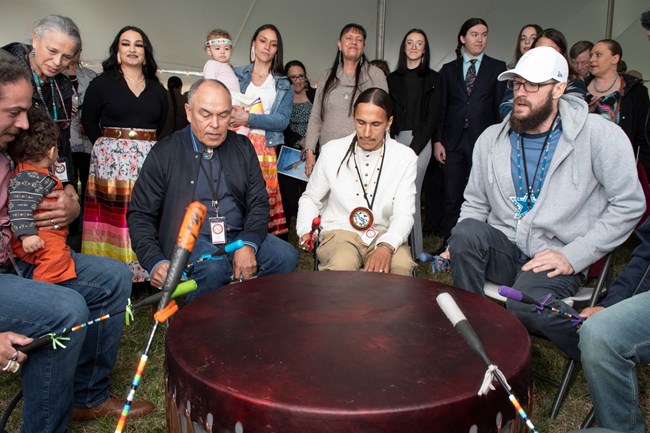 Drummers from the Rappahannock Tribe gather around a large drum to perform under a large event tent.