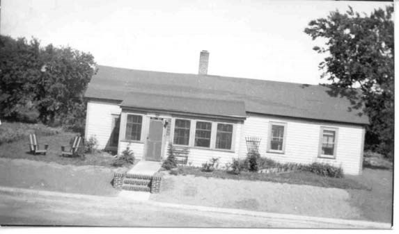 a small, white farmhouse with two chairs out front