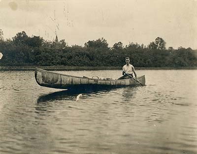A young man (Franklin Roosevelt) navigating a bay in a birchbark canoe.