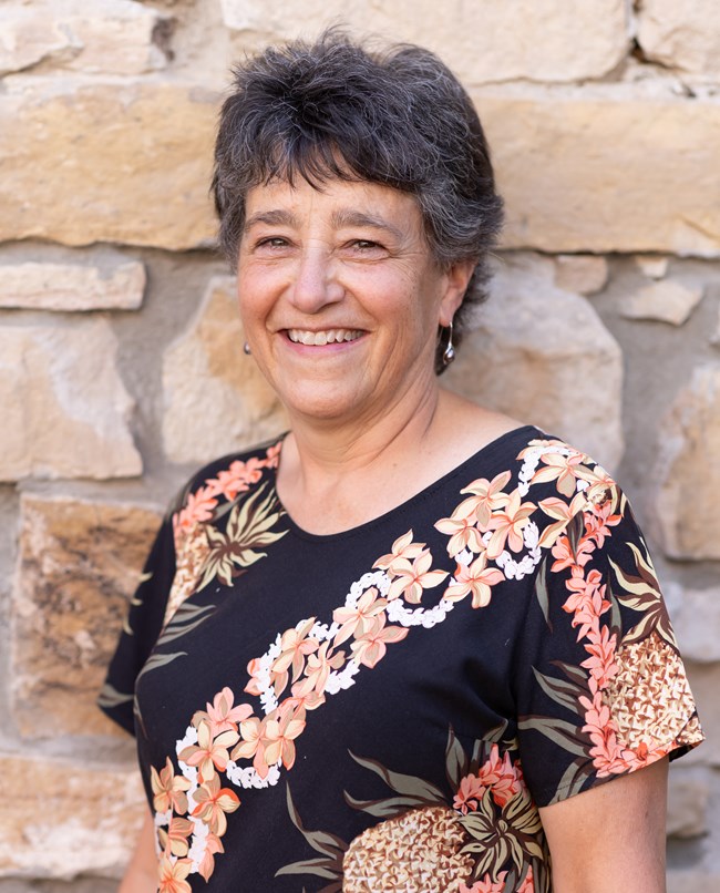 A smiling person with short hair wearing a dark colored shirt,