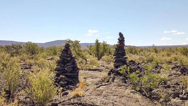 2 tall towers of stacked rocks stand on either side of a trail