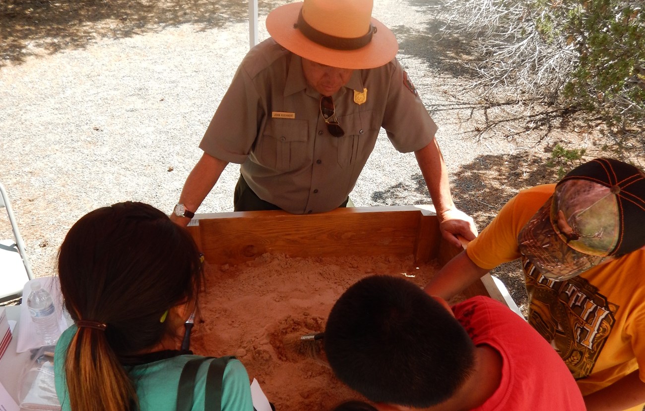 Ranger showing kids archeology tools in a mock excavation pit
