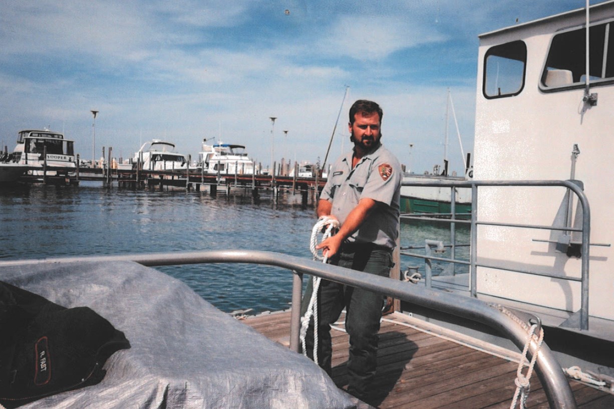 A man in uniform holds onto a boat's mooring line from a dock.