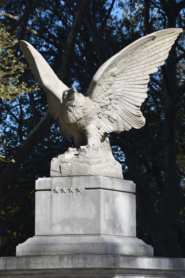 Ealge Statue Image of a white granite eagle on a pedestal with trees in the background