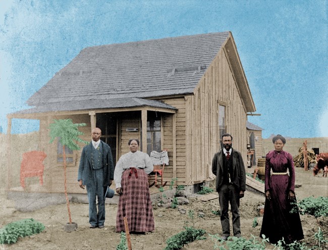 Picture of four African Americans in the 1880s posing in front of a one-story wood frame house.