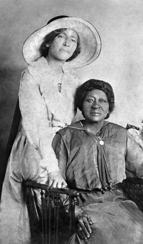 Two women, one standing, one sitting, pose for this 1910 black and white photo wiki