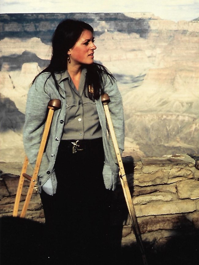 Eileen Szchowski wearing NPS uniform with her crutches stands in front of the Grand Canyon.