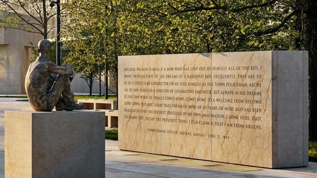 Eisenhower Young Statue back Bronze statue of Eisenhower seated as a boy from back facing large stone slap engraved with quote
