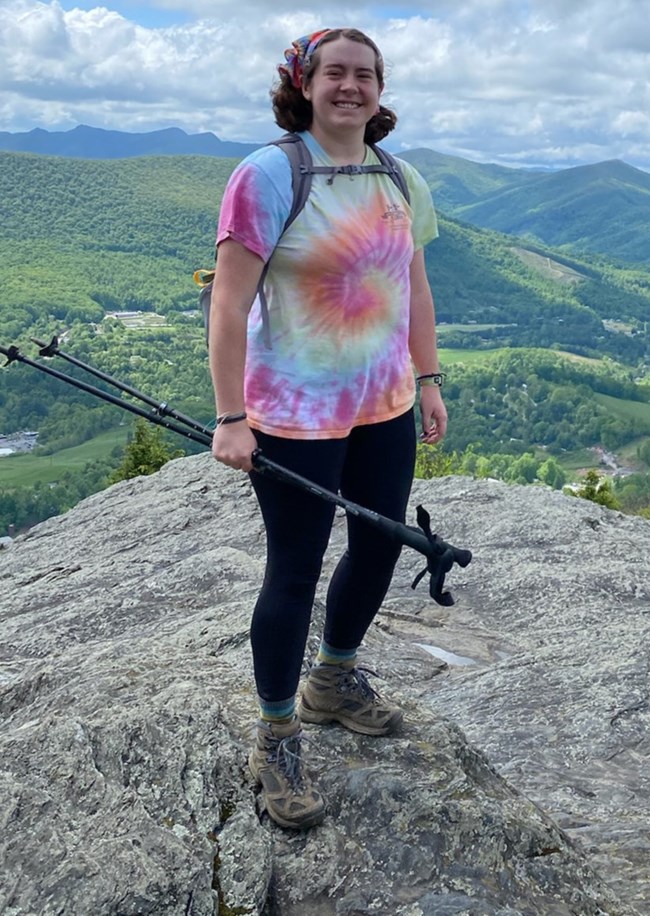 Woman holding walking sticks standing on top of a mountain