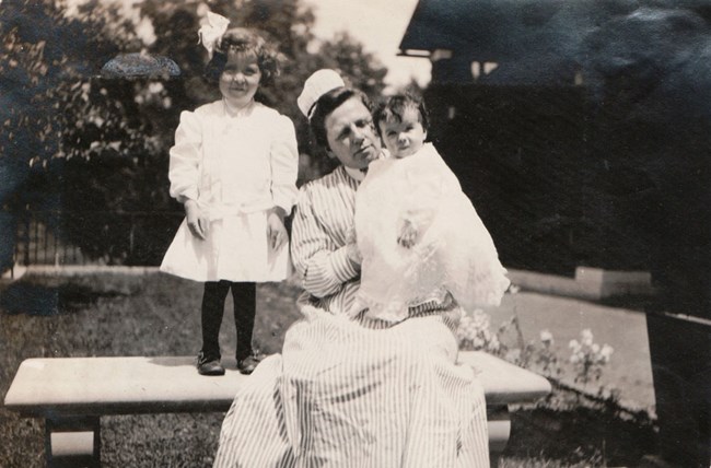 A woman with two young children. The woman is wearing a maid uniform.