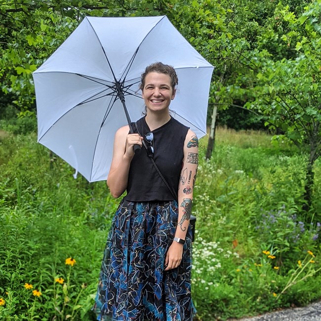 national park service intern poses in a park while holding an umbrella