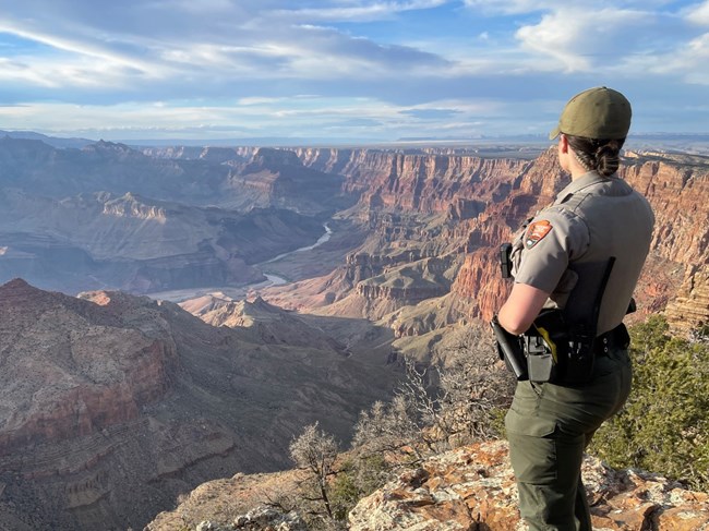 lt= A female law enforcement ranger in uniform overlooks a large, wide canyon.