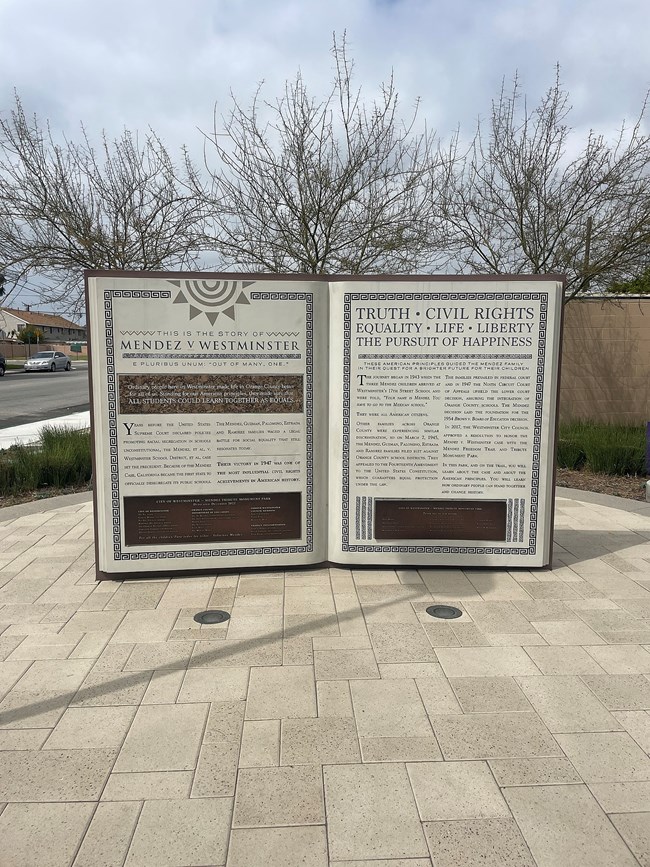 Photo of monument shaped like a giant book standing up with the pages splayed open. The inside of the book describes the story of the Mendez v. Westminster case.