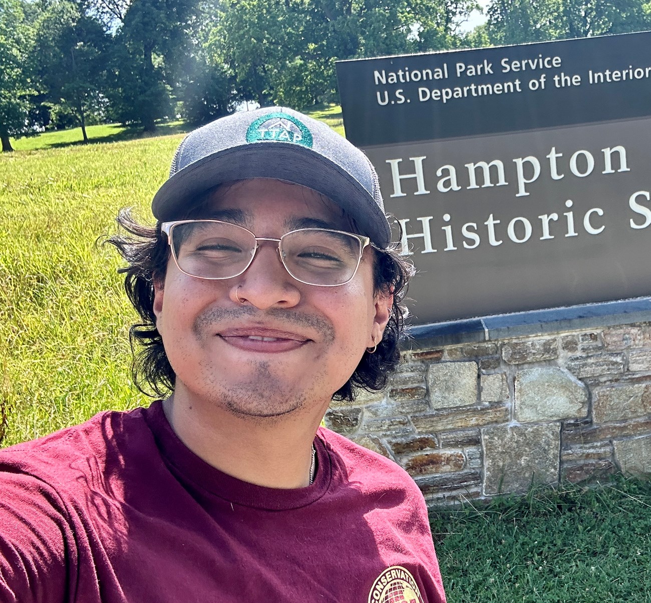 Hampton National Historic Site Landscape Stewardship Corps Intern Erick Contreras Intern Erick Contreras smiles for a selfie in front of the Hampton National Historic Site sign