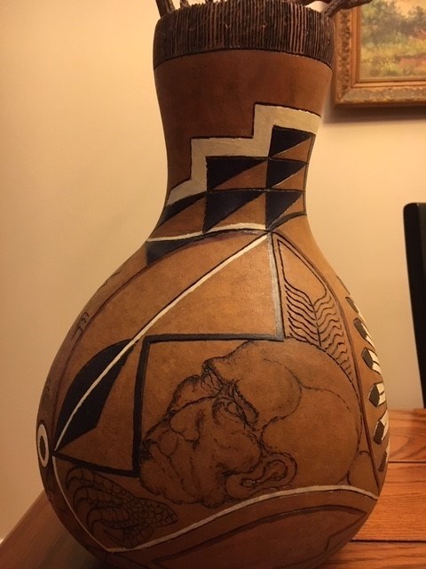 Gourd with geometric patterns and a male face painted on it.