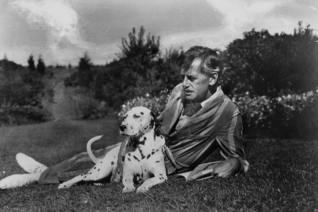 An older man lays in the grass with his dog.