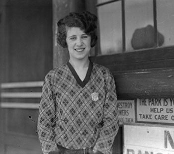 Eva McNally wearing a badge and gun holster stands on the ranger station porch.