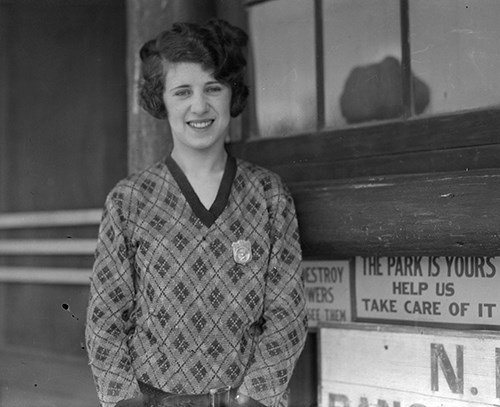 Temporary Ranger Eva McNally wears a sweater with her badge pinned to her chest.  Her short hair is curled away from her face.