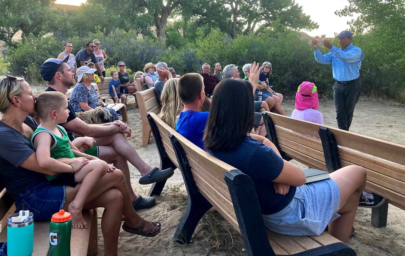 Ezparza-Limón leading an evening ranger program at the Green River Campground. Standing, he holds up two models of butterflies in front of a crowd of seated spectators.