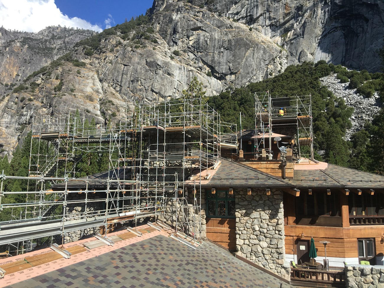 Exterior scaffolding installed on the outside of stone and wooden structure with a large granite mountain in the background.