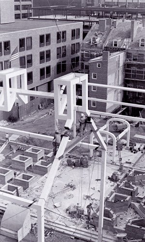 Two workers high in the air connecting the steel outline frame of Ben Franklin's house.